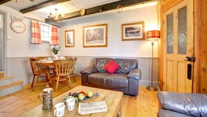 A cozy living room with a leather sofa, wooden dining table, and a coffee table with a newspaper. - 3 Bed in Whitby (oc-r020) (Robin Hood's Bay)