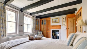 A bedroom with a large bed, a fireplace, wooden doors, and a window with curtains. - 3 Bed in Whitby (oc-r020) (Robin Hood's Bay)