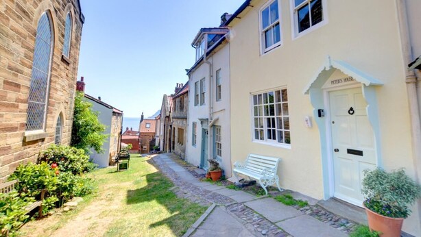 A narrow street with stone buildings, a bench, and a sign for 'Peters House'. - 3 Bed in Whitby (oc-r020) (Robin Hood's Bay)