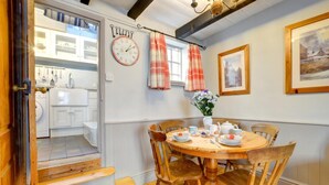 A dining area with a round wooden table, chairs, and a clock on the wall. - 3 Bed in Whitby (oc-r020) (Robin Hood's Bay)