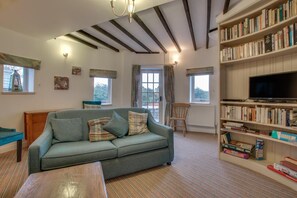 Ein gemütliches Wohnzimmer mit einem grünen Sofa, einem Holztisch, einem Bücherregal voller Bücher und einem Fernseher.