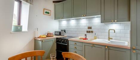 A kitchen with a dining table set for two, featuring a toaster, kettle, and a sink with a gold faucet.