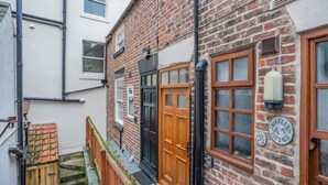 A brick building with a wooden front door, a small staircase, and a sign indicating a cottage. - 2 Bed in Whitby (oc-w794) (Whitby)