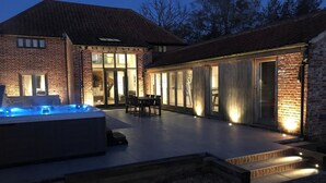 A modern house with a hot tub, outdoor seating, and a large glass door leading to a patio area. - 3 Bed in Banningham (oc-rftg) (Banningham)