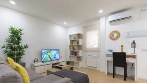 A modern living room with a grey sofa, a TV, a small table, a bookshelf, and a desk with a chair. - AR Plaza Castilla spacious and modern apartment (Madrid)