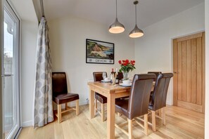 A dining area with a wooden table, leather chairs, pendant lights, and a framed picture on the wall.