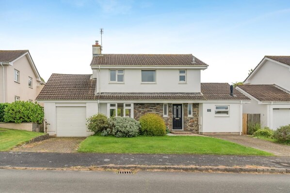 Une maison à deux étages avec un garage à l’avant, une façade en pierre et une pelouse bien entretenue.