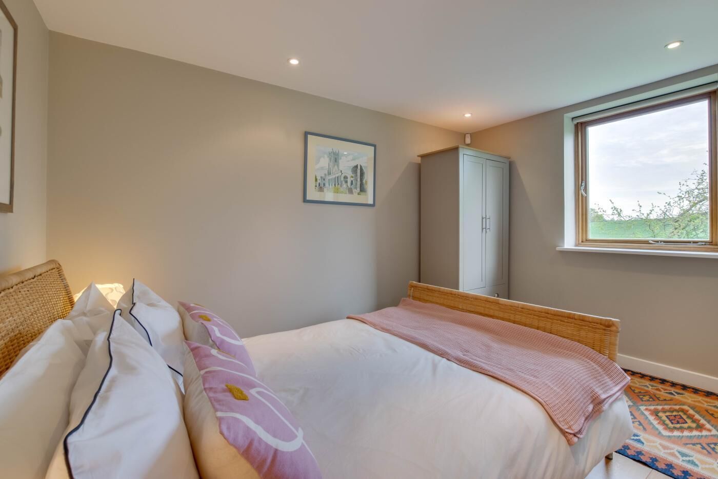A bedroom with a bed, a wardrobe, a window, and a framed picture on the wall.