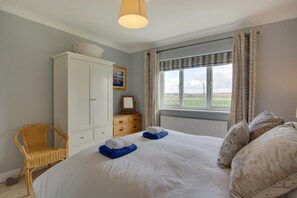 A bedroom with a large bed, a wardrobe, a window with curtains, and a view of the outdoors. - 3 Bed in Heacham (oc-2067) (Heacham)