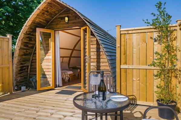 A wooden dome-shaped structure with an open door leading to a bedroom. A table with a bottle and glass is outside. - 1 Bed in Northrepps (oc-f32557) (Cromer)