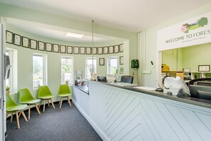 Un espace d’accueil avec un comptoir, des chaises vertes, des tableaux encadrés accrochés au mur et une enseigne sur laquelle on peut lire : « BIENVENUE CHEZ FOREST’S ».