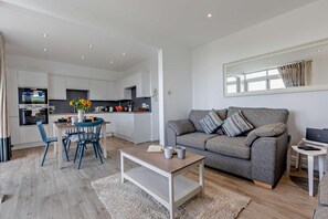 A modern living room with a grey sofa, a coffee table, and a dining area with blue chairs.