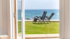 Udsigt fra en balkon over et græsareal med to liggestole, der vender ud mod vandet.