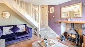 A cozy living room with a purple sofa, a fireplace, and a staircase leading to another room. - 2 Bed in Sedgeford (oc-2121) (Sedgeford)