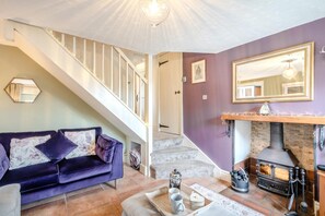 A cozy living room with a purple sofa, a fireplace, and a staircase leading to another room. - 2 Bed in Sedgeford (oc-2121) (Sedgeford)