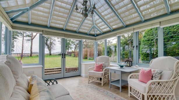 A conservatory with a glass roof, a sofa, two chairs, a table, and a view of a garden. - 3 Bed in Cley (oc-2122) (Cley next the Sea)