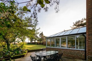 Une terrasse avec une table ronde et des chaises, un mur en briques et une véranda en verre.
