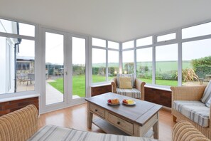 A conservatory with large windows, wicker furniture, and a table with fruit. - 4 Bed in Trevone (oc-p00863) (Trevone)