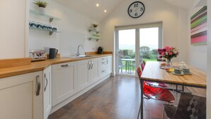 Une cuisine moderne avec des meubles blancs, un plan de travail en bois et une grande fenêtre donnant sur un jardin.