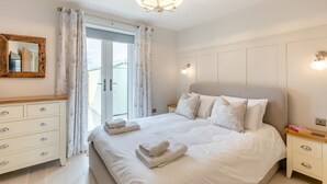 A bedroom with a large bed, a wooden dresser, a mirror, and a chandelier. - 3 Bed in Beadnell (oc-p32544) (Beadnell)