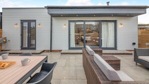 A modern house with a patio area featuring a wooden table, chairs, and a wicker sofa. - 3 Bed in Beadnell (oc-p32544) (Beadnell)