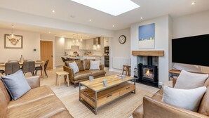 A spacious living room with a high ceiling, a fireplace, a dining area, and a kitchen in the background. - 3 Bed in Beadnell (oc-p32544) (Beadnell)