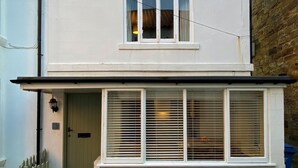 Ein zweistöckiges Wohngebäude mit weißer Fassade, einem kleinen Dachfenster und einer Haustür mit einem Zierzaun.