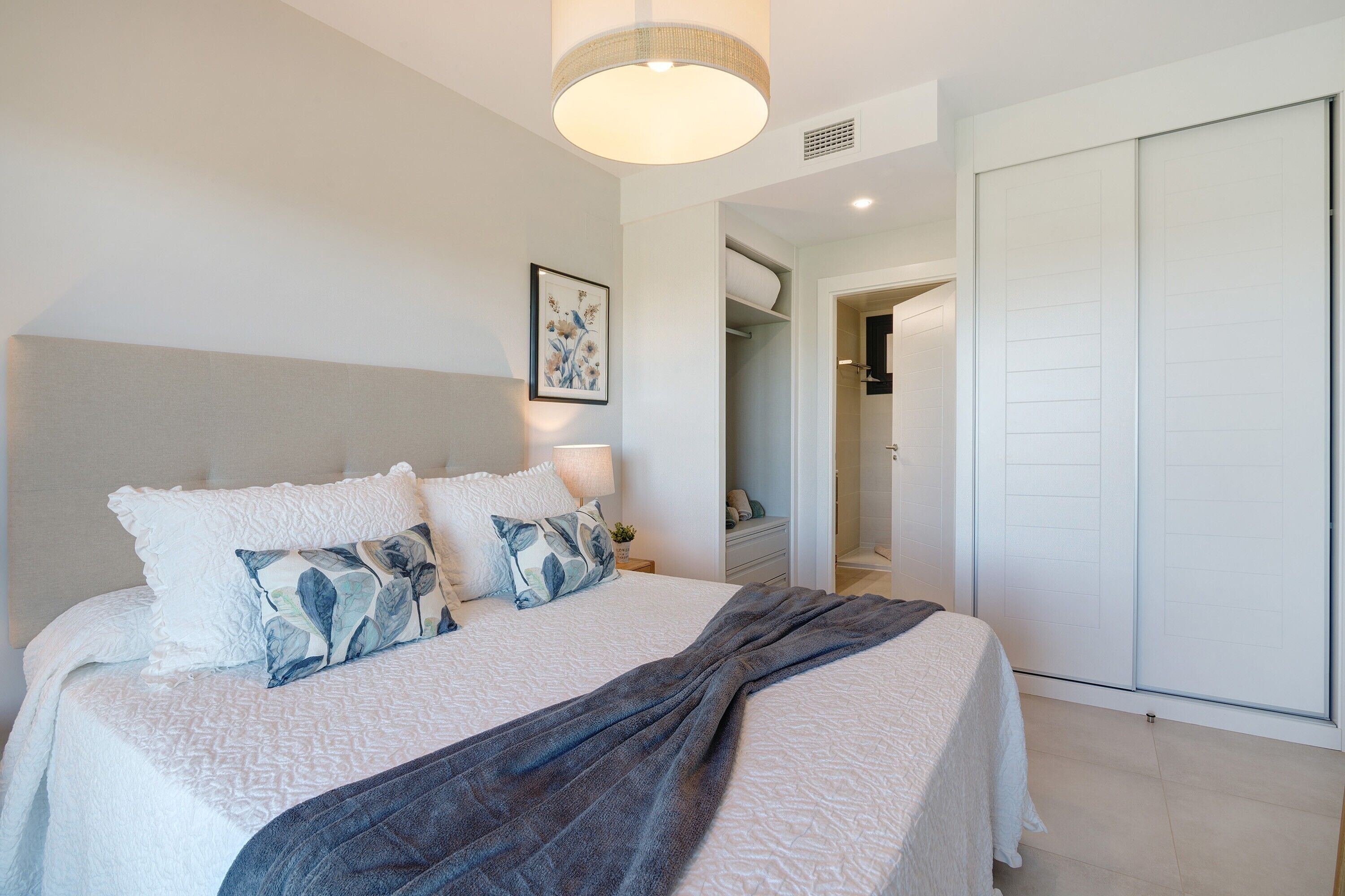 A bedroom with a bed, a bedside table, a lamp, a wardrobe, and a framed picture on the wall.