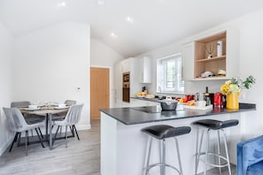 A modern kitchen with a central island, bar stools, and a dining area with a table and chairs.