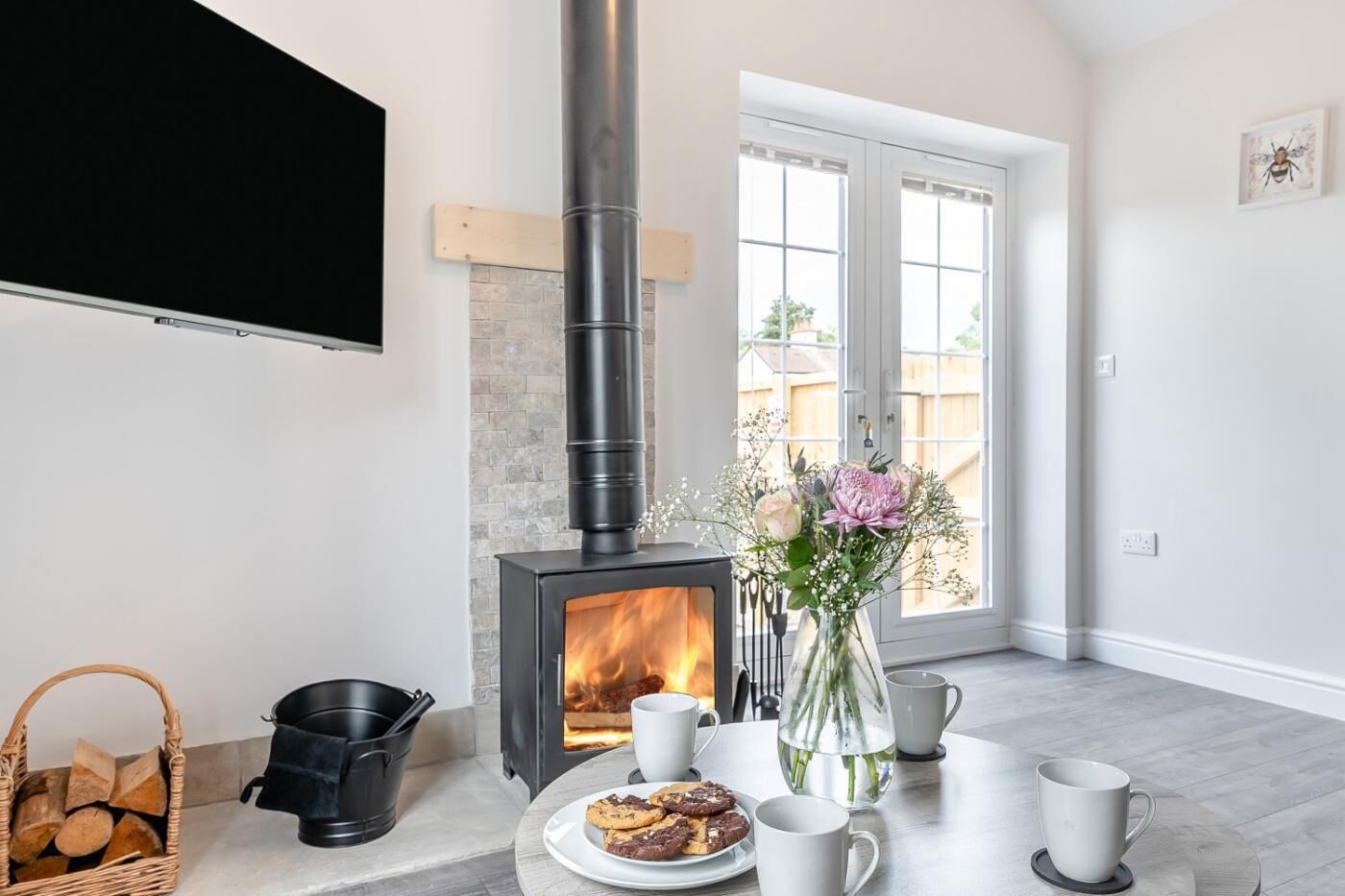 A cozy room with a fireplace, a dining table with cookies, and a vase with flowers.