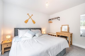 A bedroom with a large bed, bedside tables, a desk, a mirror, and two wooden paddles on the wall.