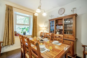 A dining room with a wooden table, chairs, a cabinet with glass doors, a clock, and a window with curtains. - 3 Bed in Hawes (oc-ds1009) (Hawes)