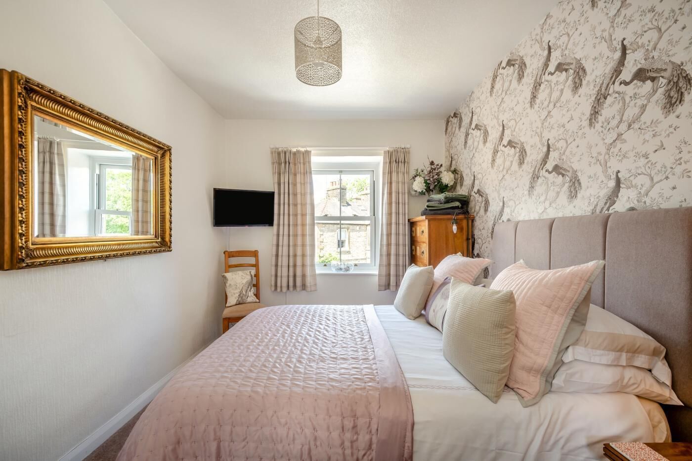 Une chambre avec un grand lit, une télévision, une fenêtre avec des rideaux et un papier peint à motifs.