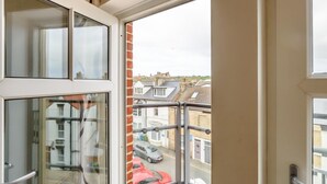 Blick vom Balkon mit Glasdoor auf eine Straße mit parkenden Autos und Wohnhäusern.