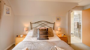 Ein ordentlich eingerichtetes Schlafzimmer mit einem Bett, zwei Nachttischlampen, einem Nachttisch und einer Tür zu einem Badezimmer.