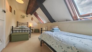 Ett sovrum med ett sluttande tak, en säng med blommigt sänglinne, ett sängbord, en lampa och ett fönster med utsikt över himlen.
