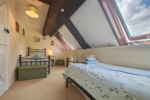 A bedroom with a sloped ceiling, a bed with floral bedding, a bedside table, a lamp, and a window with a view of the sky. - 2 Bed in Lyme Regis (oc-c32116) (Lyme Regis)