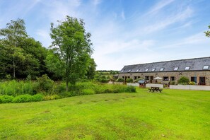 A stone building with a sloped roof, a picnic table, and a grassy area. - 2 Bed in Lyme Regis (oc-c32116) (Lyme Regis)