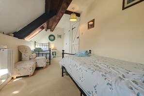 A bedroom with a bed, a chair, a small table, a radiator, and a door. - 2 Bed in Lyme Regis (oc-c32116) (Lyme Regis)