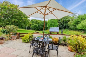 An outdoor patio with a table and chairs, a large umbrella, and a picnic table in a garden setting. - 2 Bed in Lyme Regis (oc-c32116) (Lyme Regis)
