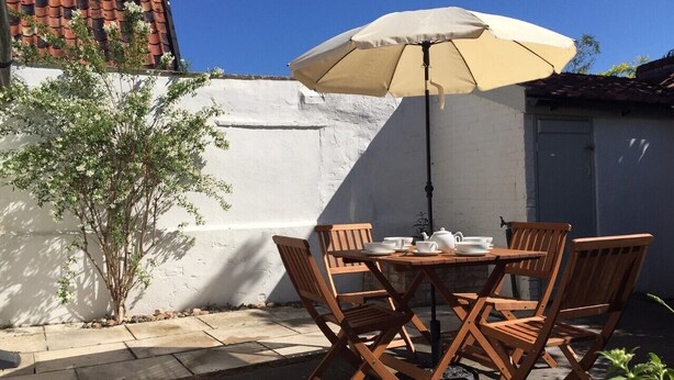 An outdoor patio with a round wooden table, four wooden chairs, a beige umbrella, and a small tree. - 2 Bed in Eye (oc-4lamb) (Eye)