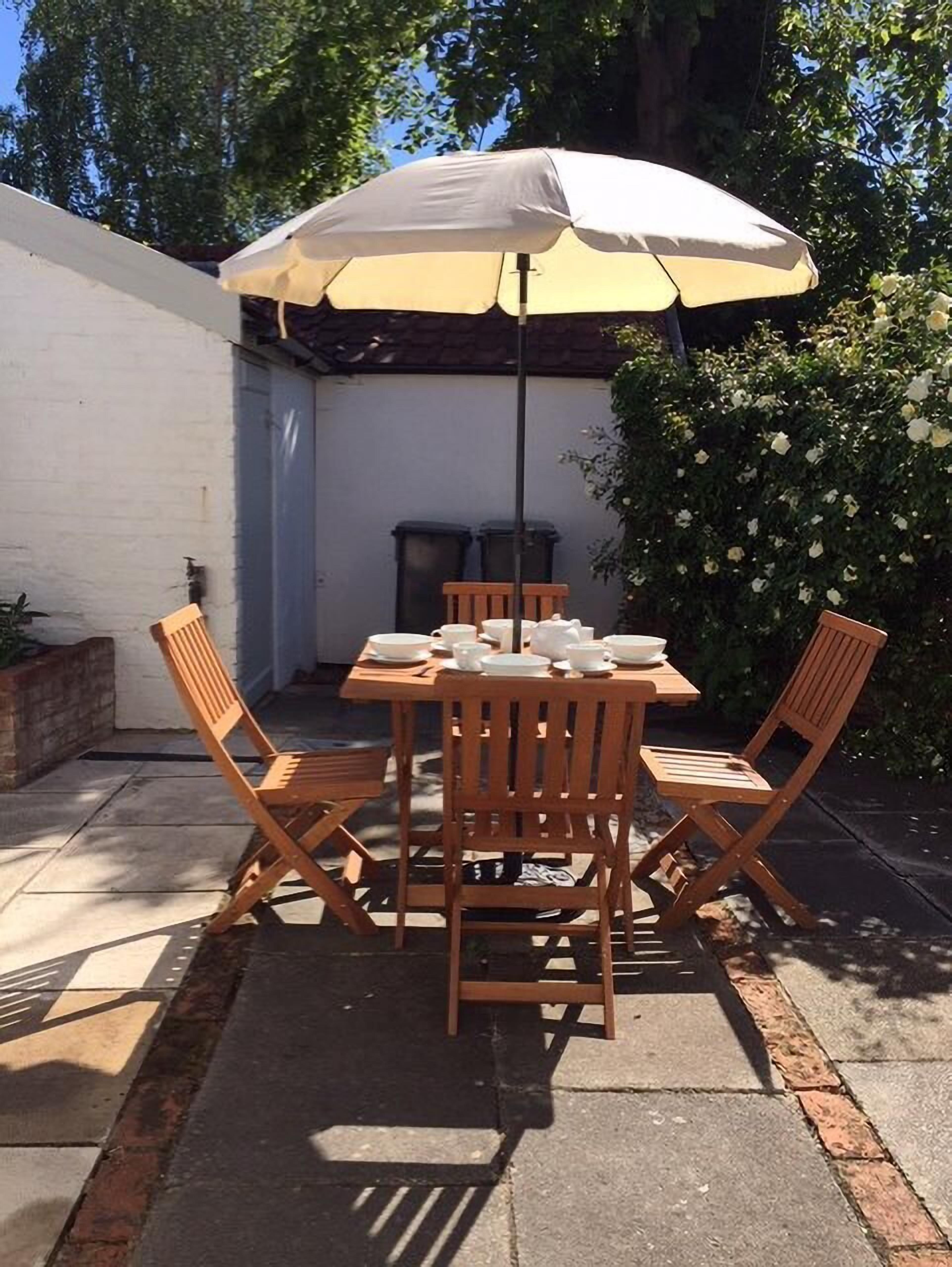 Une terrasse avec une table dressée pour quatre personnes, entourée de chaises en bois, sous un grand parasol.