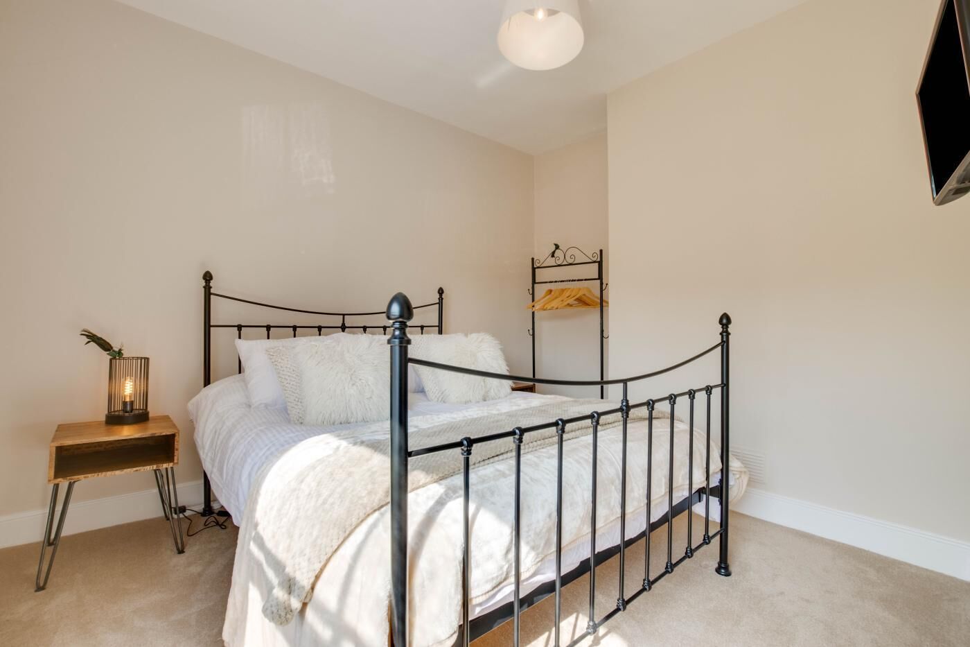 A bedroom with a metal-framed bed, a bedside table with a lamp, and a shelf with a hanging item.