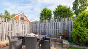 A patio with a table set for four, surrounded by wicker chairs, a wooden fence, and a brick wall. - 3 Bed in Whitby (oc-w943) (Whitby)