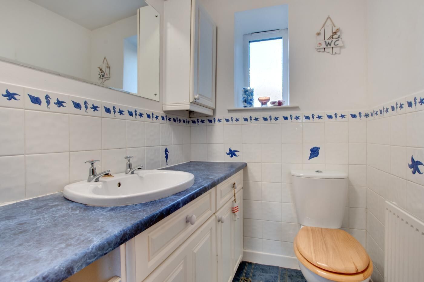Ein Badezimmer mit einem weißen Waschbecken, einer hölzernen Toilette und einer blauen Wand mit Fischmotiven.