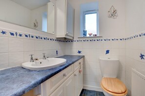 Un bagno con un lavandino bianco, un WC in legno e una parete rivestita di piastrelle blu con decorazioni di pesci.