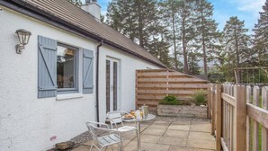 A patio with a table and chairs, a wooden fence, and a white building with shutters. - 1 Bed in Newtonmore (oc-b32417) (Newtonmore)
