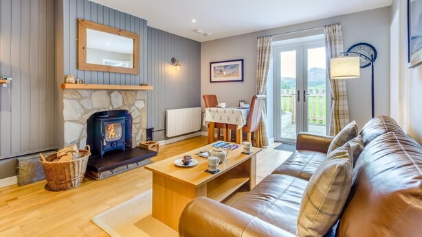 A cozy living room with a fireplace, a sofa, a dining table, and a view of the outdoors. - 1 Bed in Newtonmore (oc-b32417) (Newtonmore)
