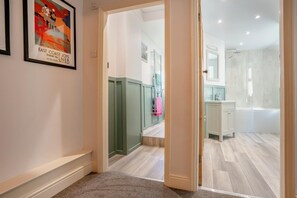 Ein Gang, der zu einem Badezimmer mit Dusche, Waschbecken und Spiegel führt.