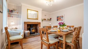 A dining room with a fireplace, wooden chairs, a table set for breakfast, and a bookshelf. - 5 Bed in Runswick Bay (oc-wa817) (Runswick Bay)